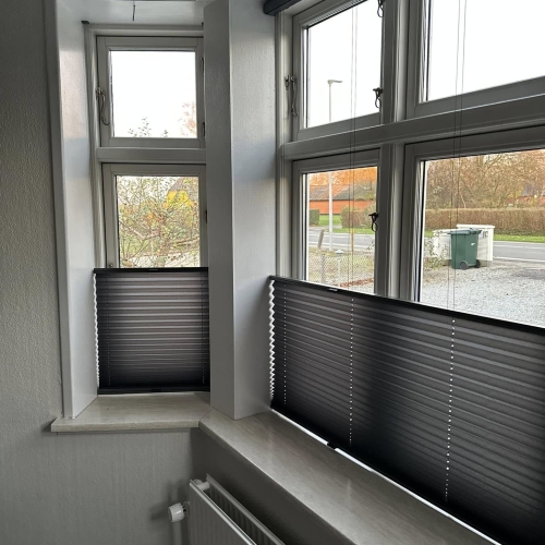 Mørke plissé gardiner monteret på stort vinduesparti i stue